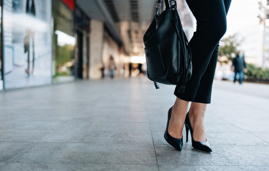 Sieviete lietišķajā tērpā, melnajās augstpapēžu kurpēs ar melnu ādas somu 