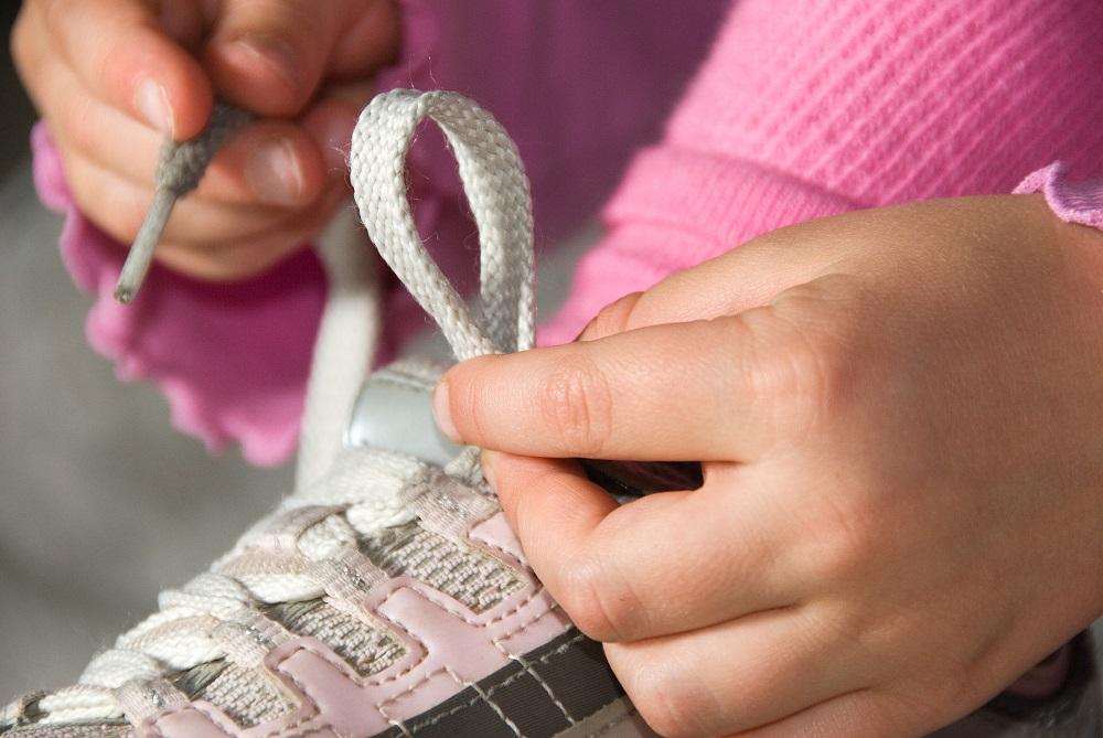 Meitene sasien bērnu šņorējamo apavu kurpju auklas