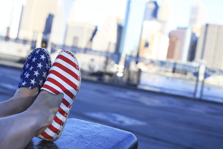 Brīvā laika apavu pāris ar amerikāņu karoga rakstu uz pilsētas fona