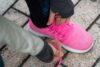 Sieviete, kurai kājās ir rozā, sieviešu snīkeri, sasien kurpju auklas