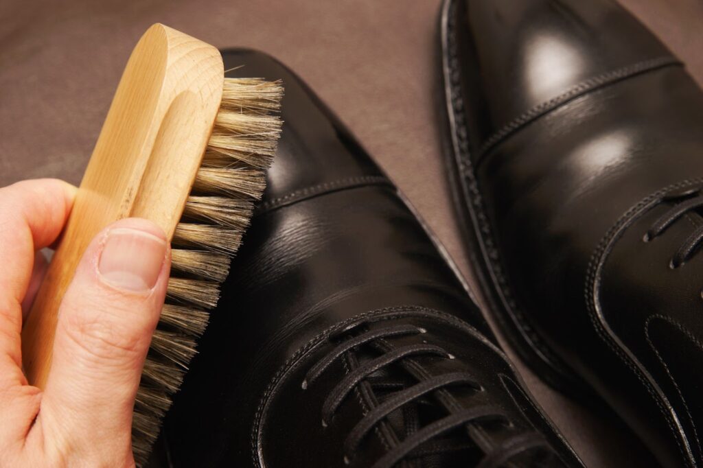 Melni, gludas ādas vīriešu izejamie apavi tiek tīrīti ar apavu birsti