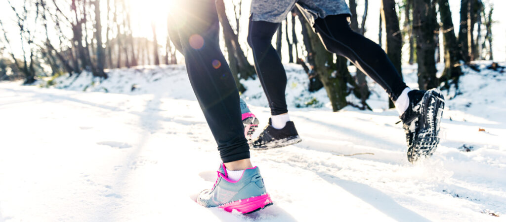 sieviete un vīrietis skrien pa aizsniegušu taku ziemas skriešanas apavos