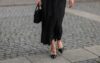 Sieviete melnajā kleitā, melnajās augstpapēžu kurpēs ar smailu purngalu
