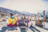 Četri jaunieši après ski stila tērpos kalnu slēpošanas kūrortā