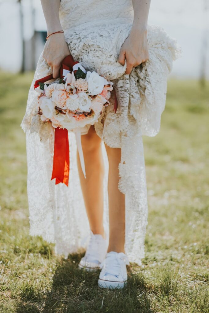 Kobieta w sukni ślubnej boho z bukietem kwiatów w dłoni ubrana w niskie białe trampki