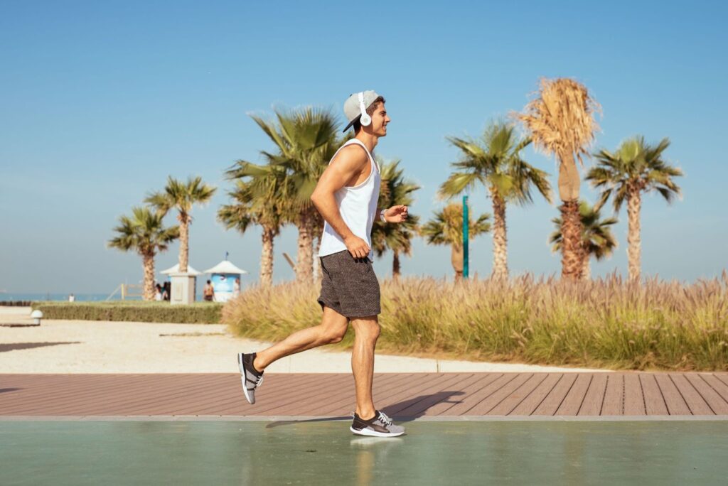 Jauns vīrietis skrien vīriešu sporta apavos. Fonā ir palmas un pludmale.