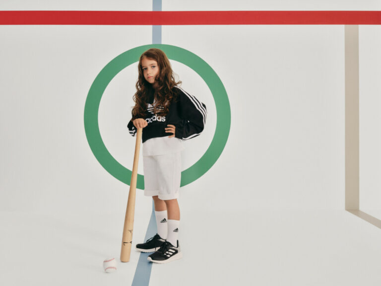 Meitene adidas zīmola sporta džemperī, baltajos šortos un melnbaltajos sporta apavos