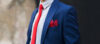 Zilās krāsas uzvalks ar sarkanu kaklasaiti un krūšu kabatas lakatiņu