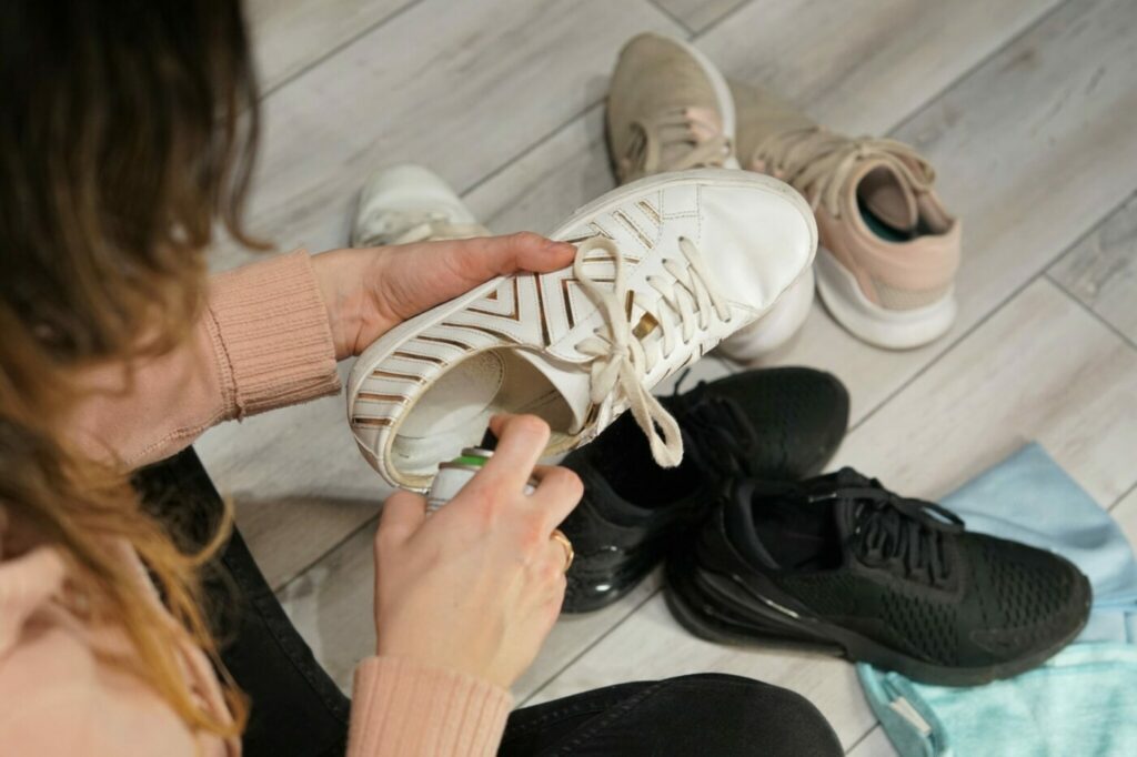 Sieviete tīra apavu iekšzoli iesmidzinot apaā apavu tīrīšanas līdzekli