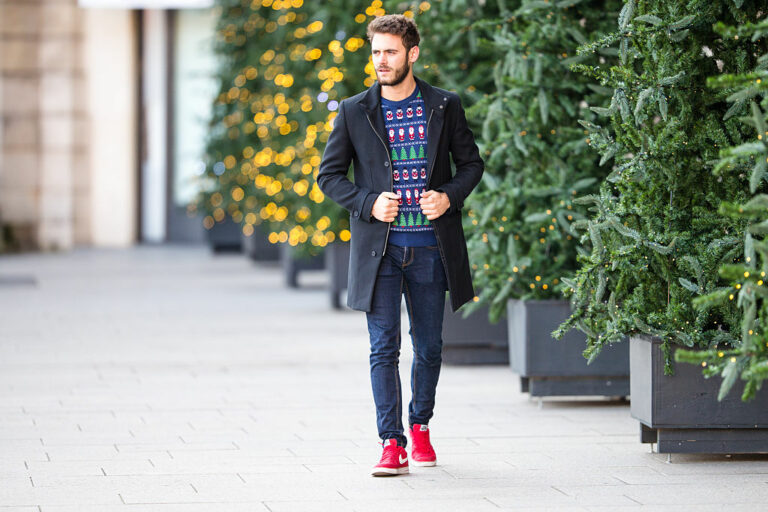 Vīrietis džemperī ar krāsainiem svētku rakstiem un sarkanos Nike zīmola snīkeros