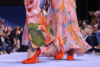 Modes sieviešu apavi SS 2024 - modeles ģērbušās puķainos tērpos un sarkanajās augstpapēžu kurpēs